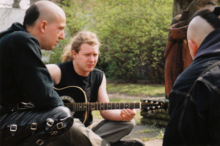 Asp und Matze mit Gitarre sitzen drauen. Im Hintergrund sind grne Strucher zu erkennen.